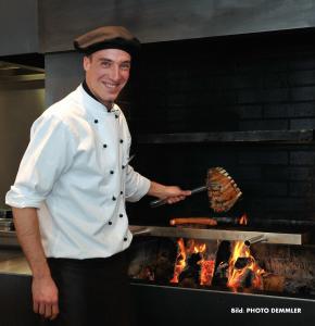 a chef is cooking meat on a grill at AUSZEIT DAS HOTEL Asbach-Bäumenheim in Asbach-Bäumenheim