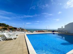 a swimming pool with chairs and the ocean in the background at Magnifique Duplex avec piscine en bord de mer in Olhos de Água