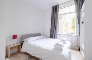 um quarto com uma cama com lençóis brancos e uma janela em Stylish 2 Bed Garden Flat in Zone 1 Central London em Londres