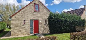 a small brick house with a red door at Lakeview 'Rotorua' 4-6 pers by Kawatea Cottages in Ewijk