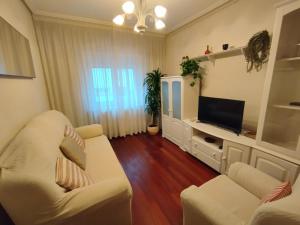 Apartamento La Luz de Reinosa 3 في رينوسا: غرفة معيشة مع كرسيين بيض وتلفزيون بشاشة مسطحة
