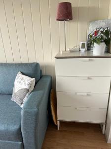 a blue couch next to a dresser with a lamp at Guest room in private house in Ålesund