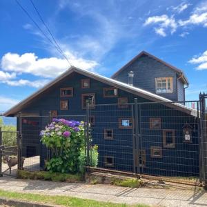 a blue house with a fence and flowers at Habitación privada, vista al mar 1 in Ancud
