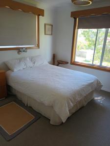 1 dormitorio con 1 cama blanca grande y ventana en Wren's Nest at Culburra Beach, en Culburra Beach