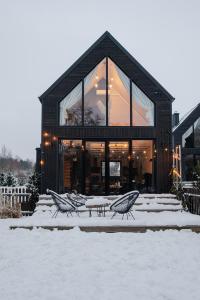 a black building with two chairs in the snow at Domki Momenty in Słajszewo