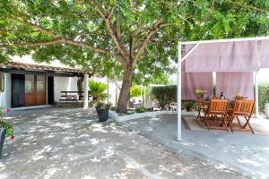 a patio with a table and chairs under a tree at Domo Anghèleda - Detached with large garden in a relaxing environment, a few minutes from the sea in Alghero