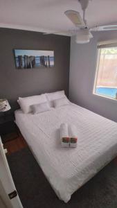 um quarto com uma cama com lençóis brancos e almofadas em Wanderlust ** Pet Friendly 3 Bedroom Home With a Pool em Sellicks Beach