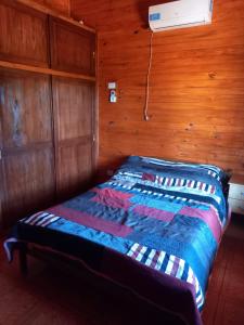 a bed in a room with a wooden wall at LA CABAÑA DE SERGIO in Gobernador Roca