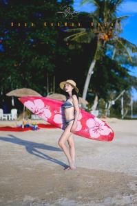 una mujer parada en la playa sosteniendo una tabla de surf en Baan Koh Mak, en Ko Mak