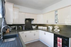 a kitchen with white cabinets and a sink at The Cottage on the Beach - Sleeps 7 - Large Garden in Penrhyn Bay