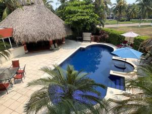 een resort met een groot zwembad met een rieten dak bij Casa Gaviota in Puerto San José