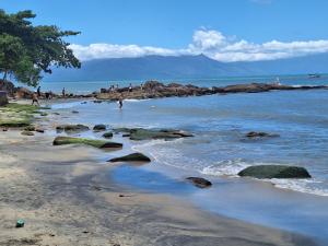 einen Strand mit Felsen und Menschen im Wasser in der Unterkunft Casa para temporada em caraguatatuba praia do Massaguaçu in Caraguatatuba