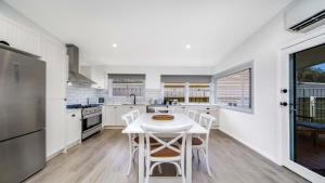 a white kitchen with a white table and chairs at Ettalong Beach House in Ettalong Beach