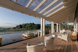 a conservatory with a deck with white furniture and a large window at Rosewood Kauri Cliffs in Matauri Bay