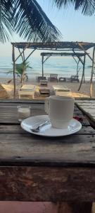 Smile Gambia Beach Bar في بروفوت: وجود كوب من القهوة على طاولة بالقرب من الشاطئ
