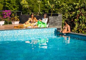 two women and a man sitting next to a swimming pool at Moustache Rishikesh Riverside Resort in Rishīkesh