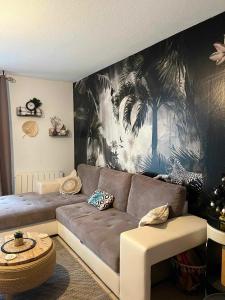 een woonkamer met een bank en een muurschildering van palmbomen bij L'Eucalyptus in Marans
