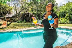 une femme tenant deux cocktails au bord de la piscine dans l'établissement Shayamoya Tiger Fishing and Game Lodge, à Pongola Game Reserve