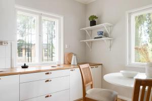 a kitchen with white cabinets and a table and two windows at Villa Merituuli - Charming Seafront Cottage in Porvoo