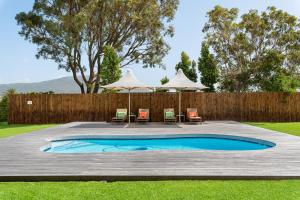 uma piscina com cadeiras e guarda-sóis num quintal em Sunset Splendour Guesthouse em Noordhoek