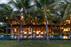 a hotel with palm trees in front of a pool at Sunset Ubud Estate with Ricefield views - RUSTERS Villa Estate in Ubud
