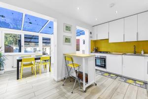 una cocina con armarios blancos y detalles amarillos en Family House in the Heart of Hanwell with 5 stars! en Londres