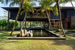een huis met een vijver en palmbomen ervoor bij Rusters Estate - Ricefield with Sunset views, Creative Spaces & Restaurant in Ubud