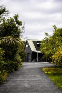 a driveway leading to a black house with a garage at Forest Waters Bungalow in Haruru