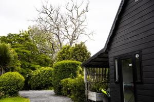 a black house with a door and some bushes at Forest Waters Bungalow in Haruru