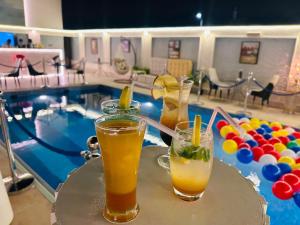 ウナイザにあるفندق شيرفل الواحة عنيزة Cheerful Al Waha Unayzah Hotelのスイミングプールの隣のテーブルでのドリンク2杯