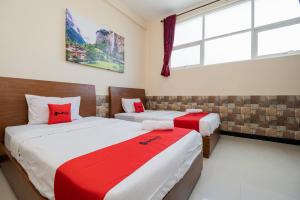 um quarto com 2 camas com lençóis vermelhos e brancos em RedDoorz Syariah near Batu Night Spectacular em Malang