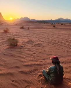 una mujer sentada en el desierto viendo la puesta de sol en Shahrazad desert, Wadi Rum, en Wadi Rum