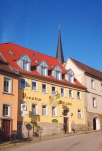 a yellow building with a red roof and a church at Pension Maintal Eltmann in Eltmann