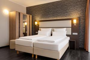 two white beds in a room with a brick wall at Amedia Express Bielefeld, Trademark Collection by Wyndham in Werther