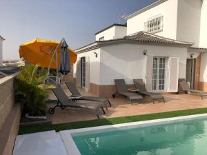 a patio with chairs and an umbrella next to a pool at Villa Vanesa luxury private villa with a heated pool, 4 bedrooms and 4 bathrooms in Adeje