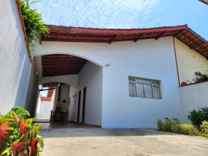 une maison blanche avec une arche et une terrasse dans l'établissement Casa no Centro 600m da Praia, à Bertioga