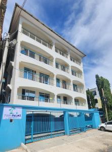 a white building with a blue fence in front of it at Twin Palms Apartments, Bamburi, Mombasa in Mombasa