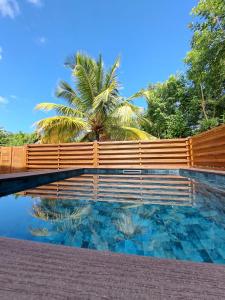 a swimming pool with a wooden fence and a palm tree at Soley'Caraibes III in Les Trois-Îlets