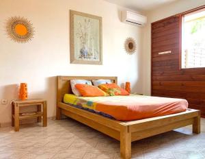 een slaapkamer met een houten bed met oranje lakens bij Gîtes Soleil étoilé - Piscine - Jardin fleuri - Terrasse in Anse-Bertrand