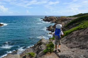 a person with a backpack standing on a cliff overlooking the ocean at Studio climatisé dans Résidence avec piscine, à proximité de la mer in La Trinité