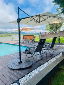 una terraza con sillas y una sombrilla junto a la piscina en Pine View Guesthouse Graskop, en Graskop