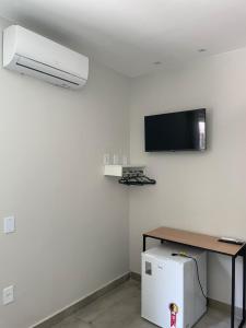 a room with a white wall with a tv and a refrigerator at Brisa dos Anjos Suítes in Arraial do Cabo