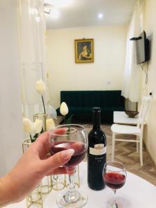a person holding a glass of wine next to a bottle of wine at Kutaisi Hotel Bzholebi in Kutaisi