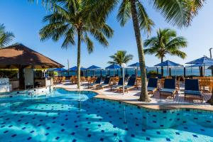 a pool with chairs and palm trees and the ocean at Hotel Vila do Farol in Bombinhas