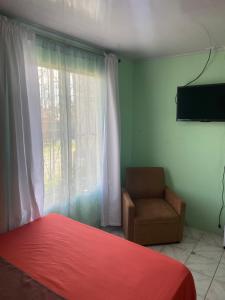 a bedroom with a bed and a chair and a window at HOSTEL CASA MARINA in Puerto Limón