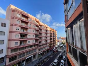 un edificio de apartamentos rosa en una calle de la ciudad con coches en Centro Santa Cruz, amplio, luminoso, a minutos de la playa., en Santa Cruz de la Palma