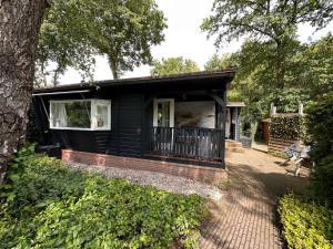 una pequeña casa negra con porche en Private Big Garden double Chalet with Outside HOTTUB and BARRELSAUNA, Woodside, Nature en Voorthuizen