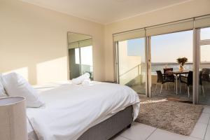 a bedroom with a large white bed and a balcony at Sea Spray A308 by Host Agents in Bloubergstrand