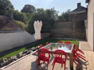 Amné-en-Champagne的住宿－Gite de charme avec piscine intérieure，庭院里配有一张桌子、红色的椅子和一把遮阳伞