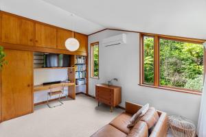 sala de estar con sofá, escritorio y ventanas en Treetop Sanctuary - Titirangi Holiday Home en Auckland